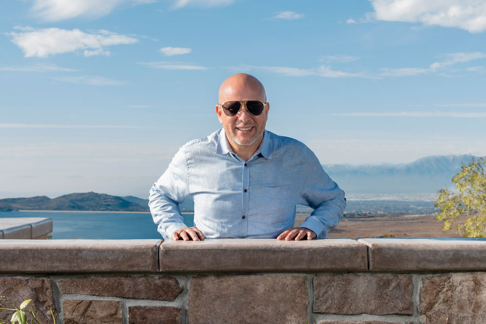 Salvador Barba, wearing sunglasses, leans over a brick wall on a ranch property over Lake Mathews